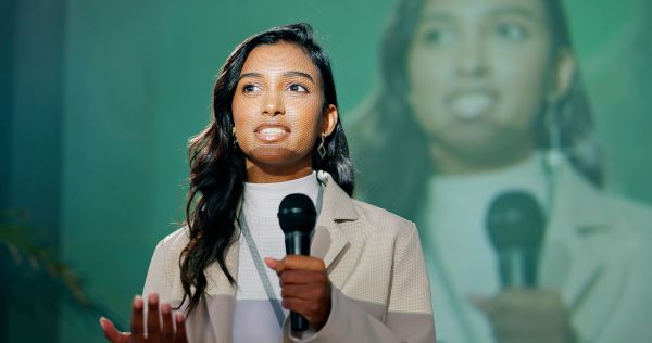 A young woman standing in front of a screen while speaking into microphone at public presentation