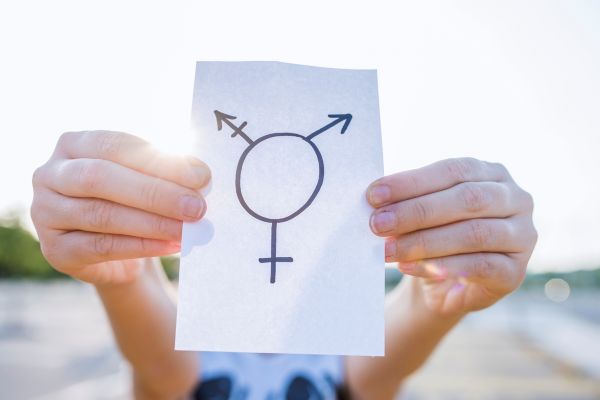 Closup of a person holding a piece of paper with the transgender symbol on it in front of face