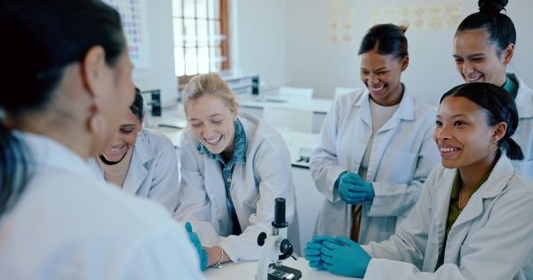 Group of students wearing lab coats and gloves listening to teacher in classroom lab