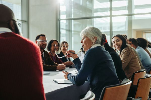 Professionals sitting around a table listening to female professional lead discussion