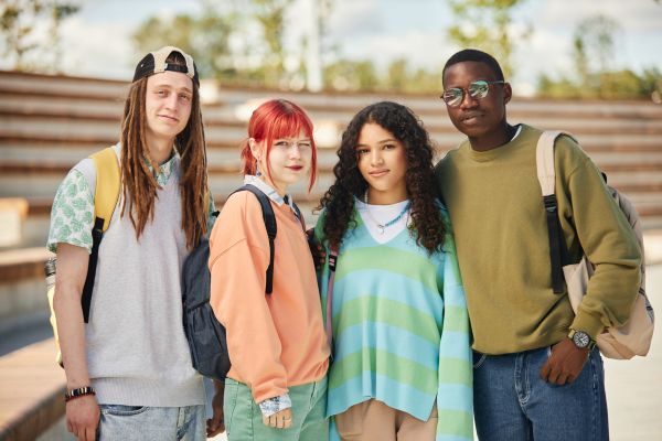 Four teens smiling and standing together outside an outdoor auditorium