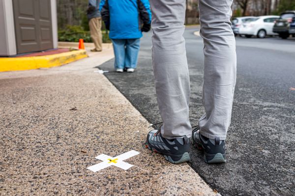 Closeup of person's legs standing near taped X on ground practicing social distancing