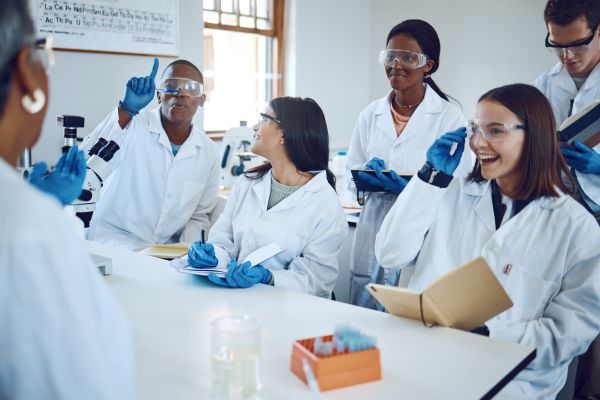 Group of high school students in lab coats and gloves gathered near teacher in classroom lab