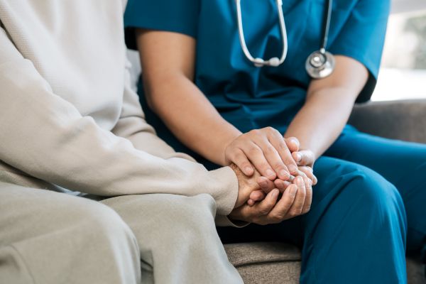 Closeup of a nurse holding a patient's hand while sitting in a hospital