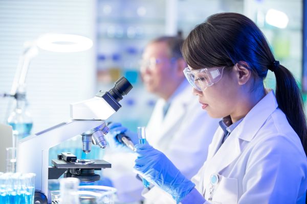 A scientist looking at a microscope while holding a test tube