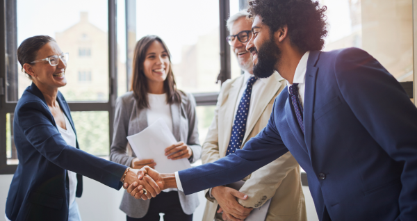 Two professionals shaking hands with two other professionals standing near