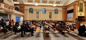 A large room with rows of seated people facing right